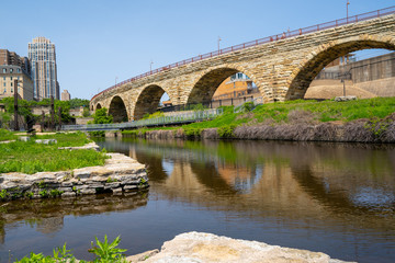 Naklejka premium Cityscape scene of downtown Minneapolis, as seen from Mill Ruins Park. View of the Stone Arch bridge on sunny spring day