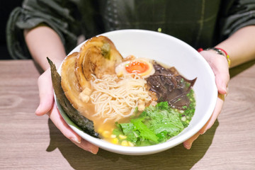 Ramen or Japanese noodles topping with Chashu or boiling pork, onions and scallions in clear soup served in a bowl on brown wooden table
