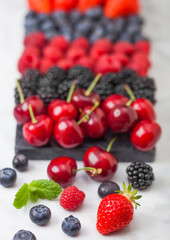 Fresh organic summer berries mix on black marble board on light kitchen table background. Raspberries, strawberries, blueberries, blackberries and cherries. Space for text