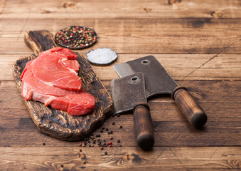 Fresh raw organic slice of braising steak fillet on chopping board with meat hatchets on wooden background. Salt and Pepper