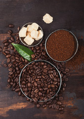 Fresh raw organic coffee beans with ground powder and cane sugar cubes on wooden background.