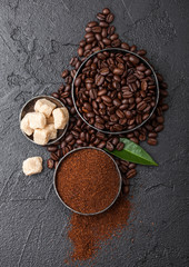 Fresh raw organic coffee beans with ground powder and cane sugar cubes with coffee trea leaf on black background.