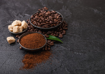 Fresh raw organic coffee beans with ground powder and cane sugar cubes with coffee trea leaf on black background.
