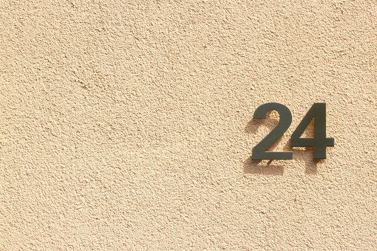 House number 24 with the twenty-four in silver with a shadow on a light orange outside wall