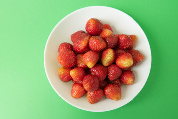 summer berry. juicy red strawberries on white plate on green background. Delicious breakfast snack. Vegetarian food. useful vitamins. isolated.