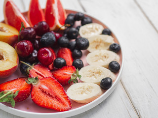 Plate with fresh summer fruits. Strawberry, blueberry, sweet cherry on wooden white background