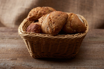 fresh baked buns in wicker basket on wooden table with sackcloth on background