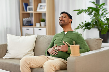 eating, consumption and people concept - full and pleased indian man enjoying takeaway food at home