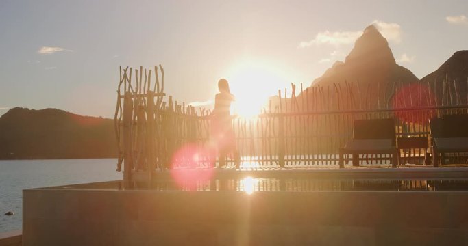 Luxury resort high end hotel rich people lifestyle woman tourist relaxing watching sunset on private balcony terrace of overwater bungalow suite in Bora Bora, Tahiti, French Polynesia.