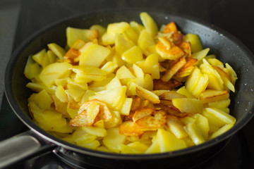 Fried potatoes in a frying pan on stove. Homemade cuisine. Potatoes is frying on stove.