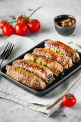 Meat rolls stuffed with Champignon served with tomatoes and green onions in heat-resistant black dish on a gray background.