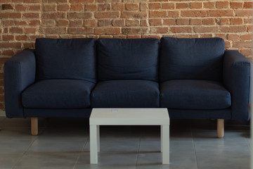 Modern living room interior. Soft sofa with white coffee table near brick wall background. 