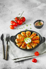 Russian stuffed cabbage rolls served with tomatoes, green onions and sour cream in heat-resistant black dishes on a gray background.