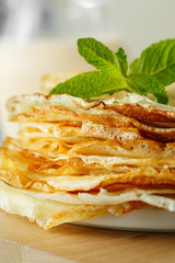 Russian pancakes served with mint leaves and ingredients - milk and eggs in front of grey background.