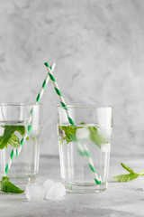 glasses of cold water with fresh mint leaves and ice cubes on grey concrete background