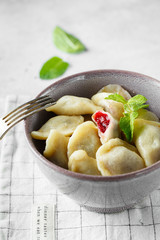 Cherry dumplings with mint. Homemade sweet dumplings with berries in the bowl on the grey background. Delicious dumplings with cherries.