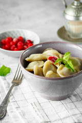 Cherry dumplings with mint. Homemade sweet dumplings with berries in the bowl on the grey background. Delicious dumplings with cherries.