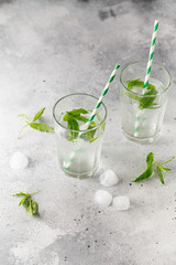 glasses of cold water with fresh mint leaves and ice cubes on grey concrete background