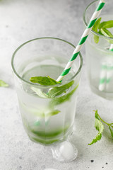 glasses of cold water with fresh mint leaves and ice cubes on grey concrete background