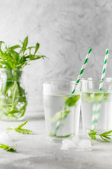 glasses of cold water with fresh mint leaves and ice cubes on grey concrete background