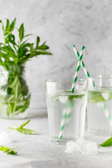 glasses of cold water with fresh mint leaves and ice cubes on grey concrete background