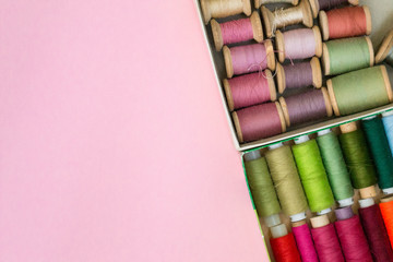 Colorful sewing threads lie in a box in a row gradient on a green background, selective focus. There is a place for text.