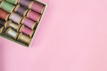 Colorful sewing threads lie in a box in a row gradient on a green background, selective focus. There is a place for text.