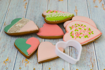 Pink and colored gingerbread and honey cakes and heart-shaped cookies lie in a messy pile on a light wooden background. Nearby are white molds for baking. Place for text. The concept of love, mother's
