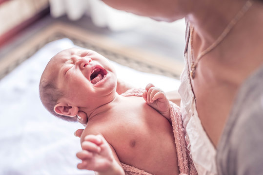 Selected focus on little lovely baby girl crying while mother try to wear her a blanket and clothes.