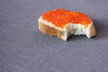 Bitten off Sandwich with red caviar on a gray background.