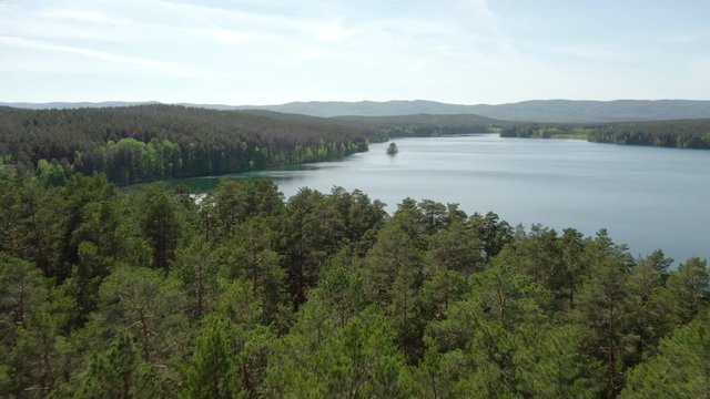 Aerial view; drone flying forward over the trees crones to horizon line; beautiful mixed forest with pine trees, bright juicy spring foliage of birches; lakes in the protected national Iremel reserve