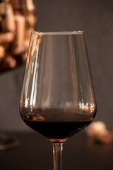 Glass of wine in the foreground with corks from the bottles inside a vase simulating a glass of wine in dark tones background