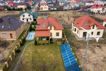 Aerial top view of residential area with new houses with roof solar photo voltaic panels, wind turbine mill and stand-alone exterior solar panel systems. Renewable green energy generation concept.
