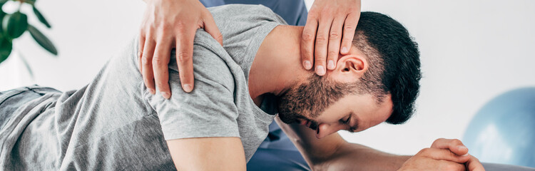 Panoramic shot of chiropractor massaging neck of lying man