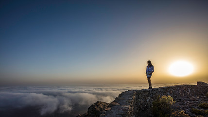 a woman on top of a mountain above the clouds during sunset