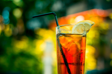 Cold ice tea in a glass with ice cubes and a black straw on a table at the bar