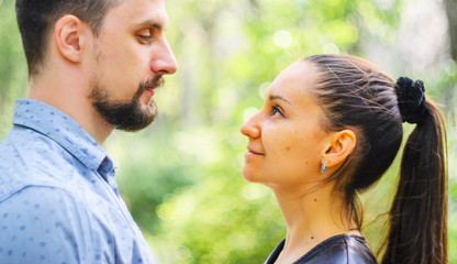 Obraz premium Outdoor portrait of a couple in love. Man and young woman with long ponytail hair look at each other