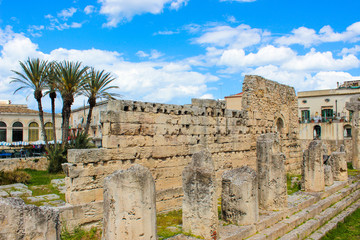 Fototapeta na wymiar Significant ancient Greek ruins of the Temple of Apollo in Ortigia Island, Syracuse, Sicily, Italy. Colonnade remnants. Palm trees in background. Sunny day, blue sky. Popular tourist place