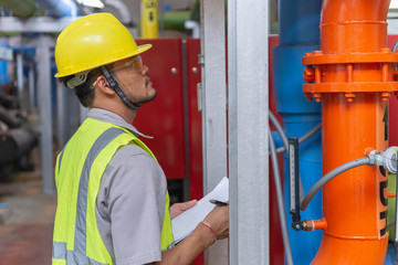 Asian engineer wearing glasses working in the boiler room,maintenance checking technical data of heating system equipment,Thailand people