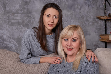 Portrait of mature woman and her daughter on sofa in living room. Happy beautiful older mother and adult daughter