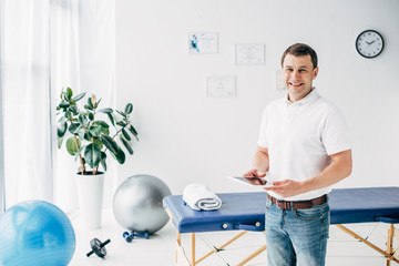 smiling chiropractor holding Digital Tablet in hospital and looking at camera