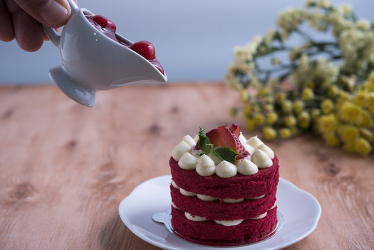 Piece of red velve cake on white plate decorated with strawberries put on the wood table.