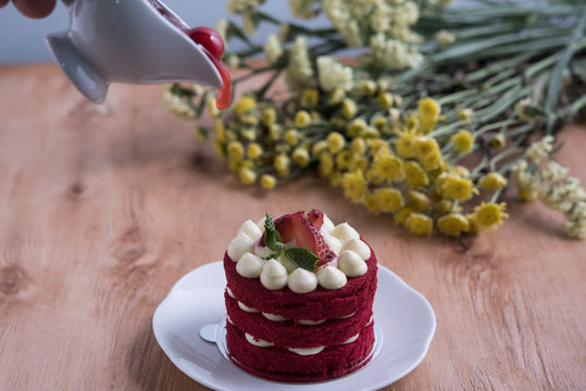 Piece of red velve cake on white plate decorated with strawberries put on the wood table.