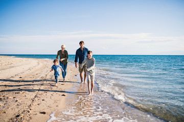Young family with two small children running outdoors on beach.