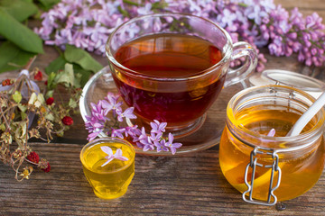 a jar of fragrant flower honey. Honey saved and lilac flowers. Cup of black tea.