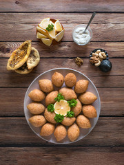 Delicious fried kibbeh with yogurt sauce in a bowl served on a plate on old wooden table. Classic Lebanese recipe