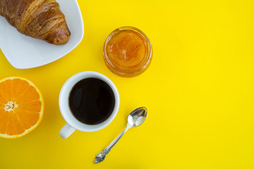 Continental breakfast with coffee, orange marmalade and  croissant on the yellow background.Top view.Copy space.