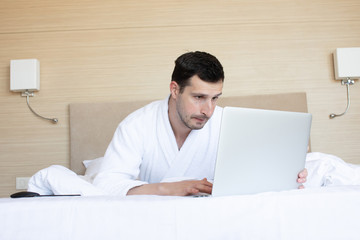   Сохранить Скачать изображение для предпросмотра Portrait of relaxed casual young man using laptop in bed at home