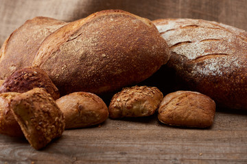 selective focus of fresh baked buns and bread on wooden table with sackcloth on background