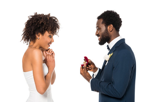african american man holding box with ring while making proposal to surprised woman isolated on white